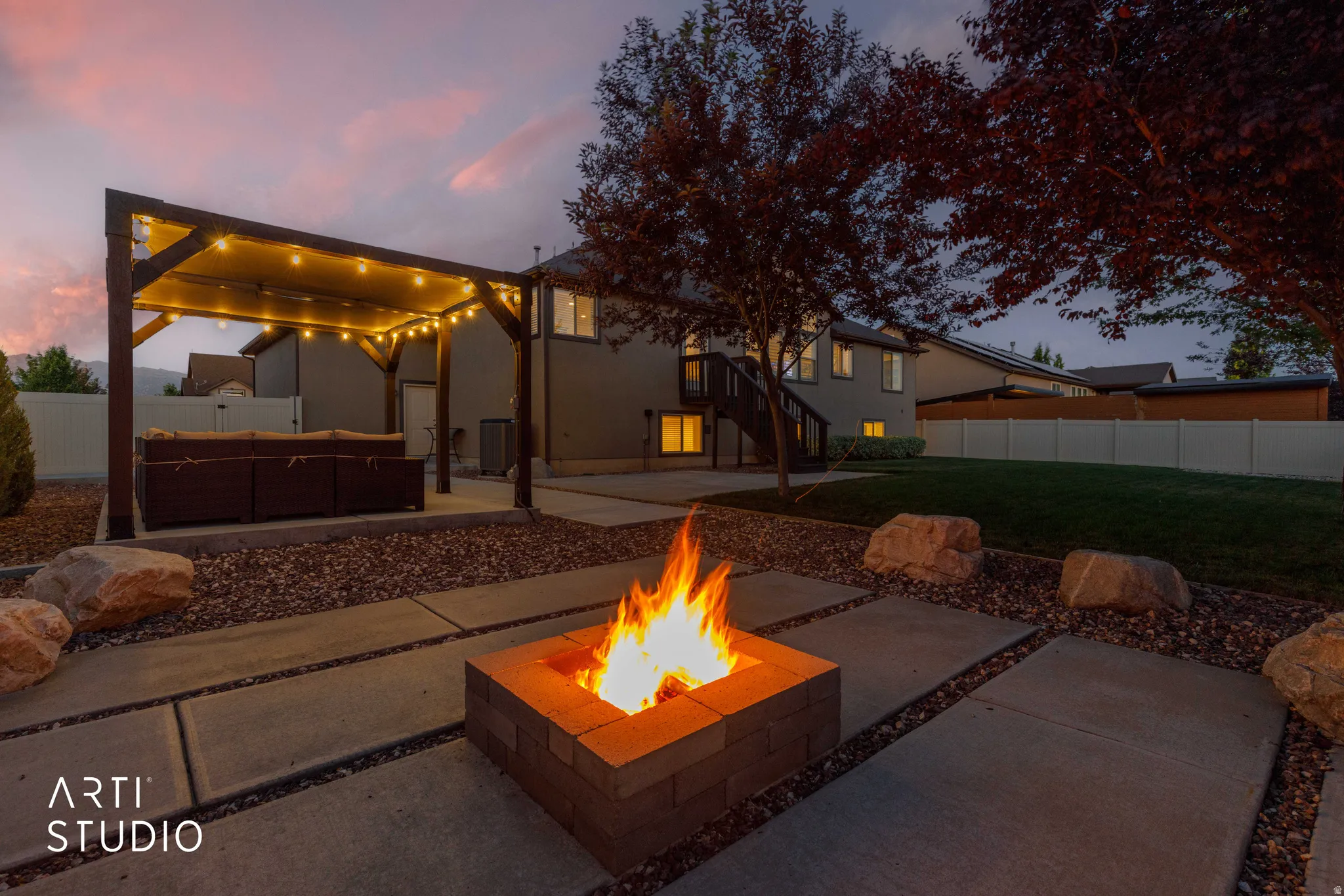 Outdoor living area featuring a stone fire pit, extensive concrete patio, and a covered pergola with string lighting