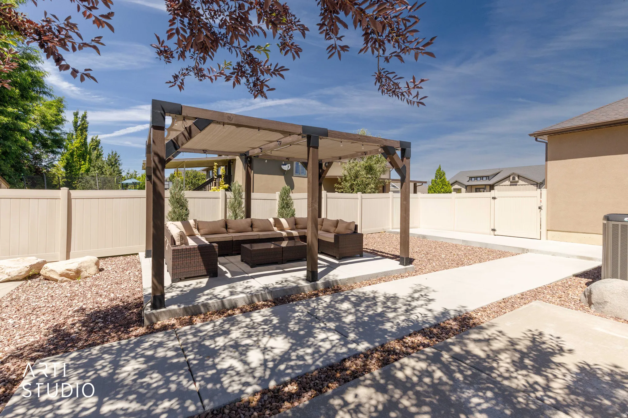 Backyard featuring a wood-frame pergola with a fabric canopy, concrete patio, gravel landscaping, and a vinyl privacy fence