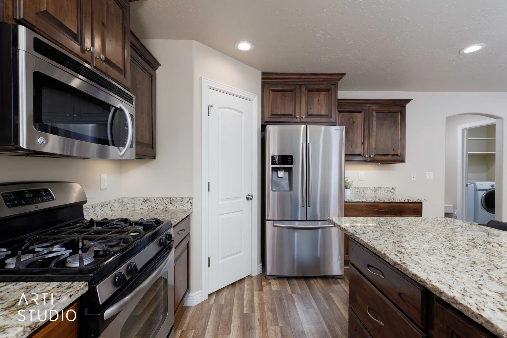 Kitchen featuring wood-finish flooring, dark wood cabinetry, light-toned countertops, stainless steel appliances, and recessed lighting