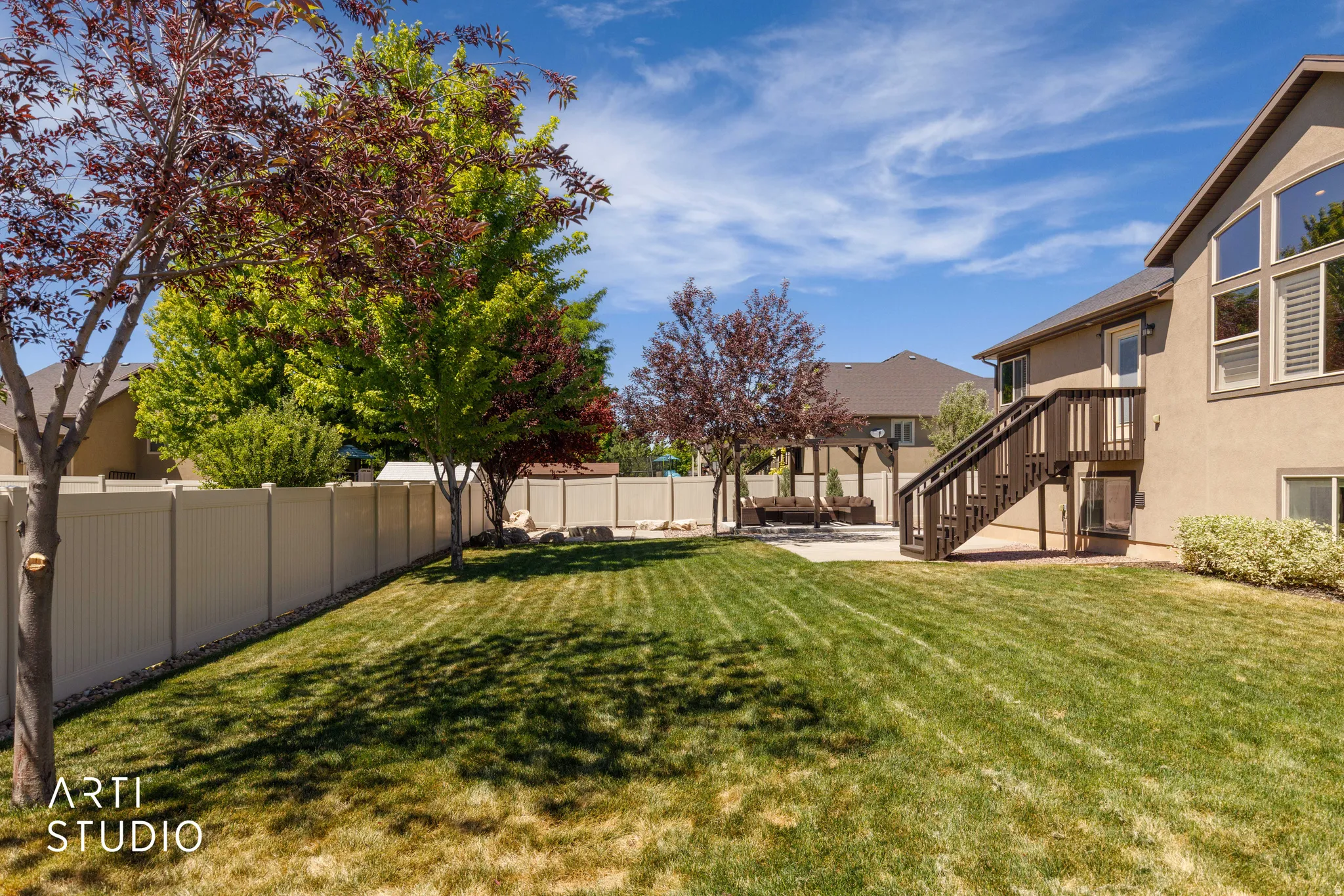 Expansive backyard featuring a manicured lawn, perimeter fencing, mature trees, and a concrete patio with a pergola