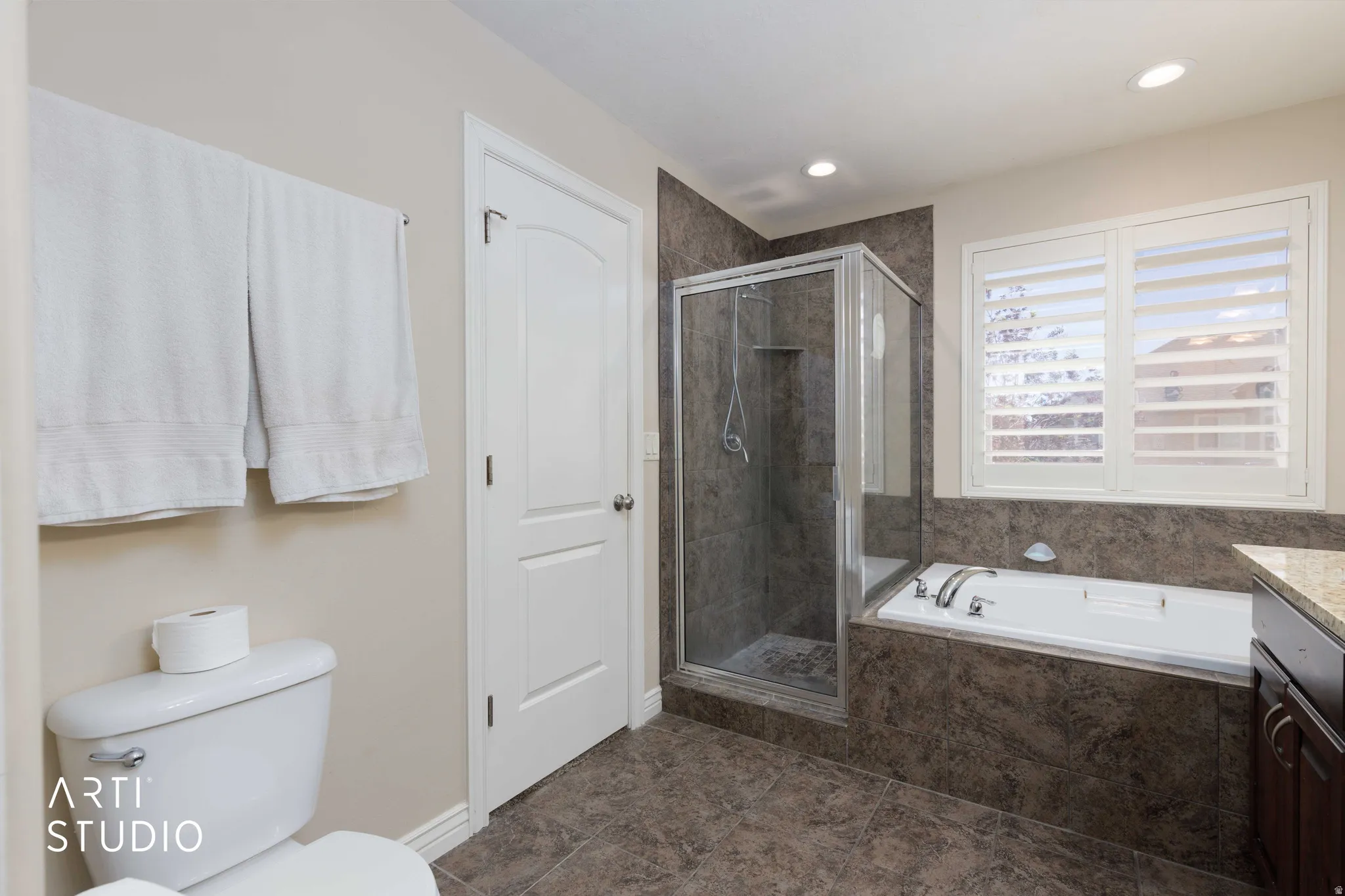 Bathroom featuring a walk-in shower with glass enclosure, separate soaking tub, and a window with plantation shutters