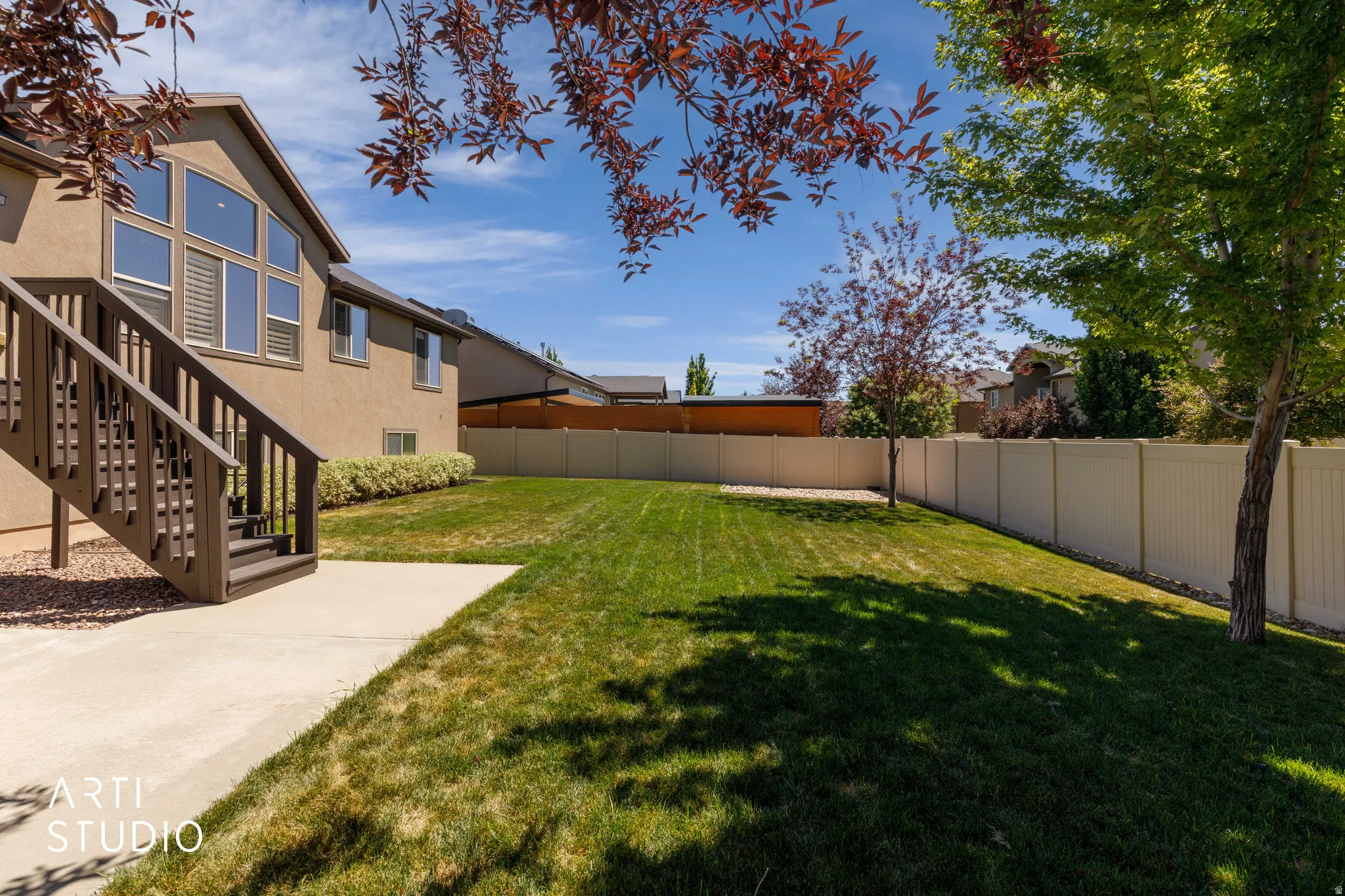 Expansive backyard featuring a manicured lawn, concrete patio, and a privacy fence