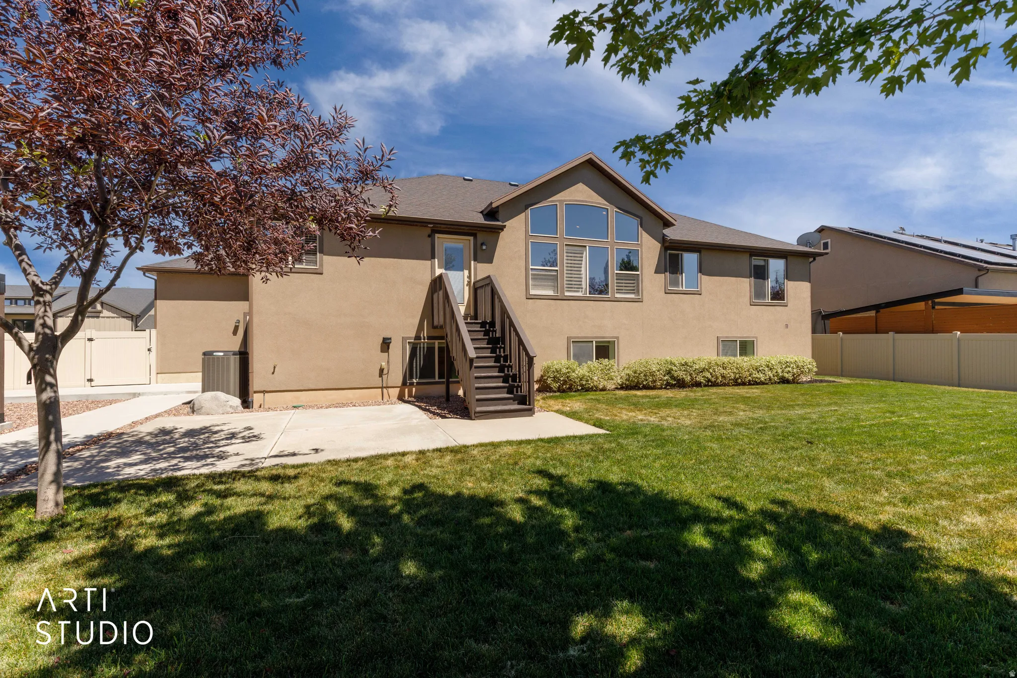 Rear exterior featuring a large lawn area, a staircase leading to an upper-level door, and a prominent multi-pane window configuration