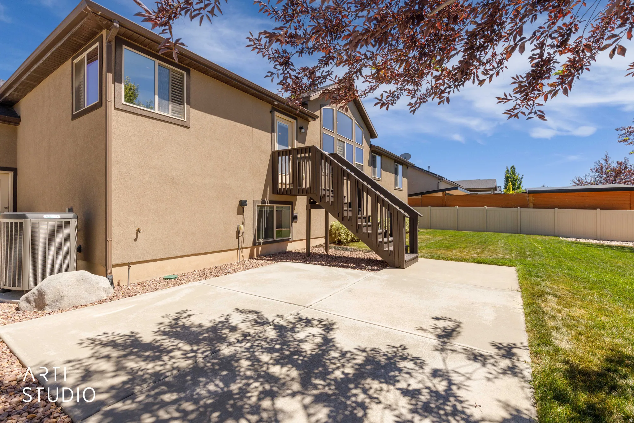 Expansive concrete patio area with a wooden staircase leading to an upper-level door
