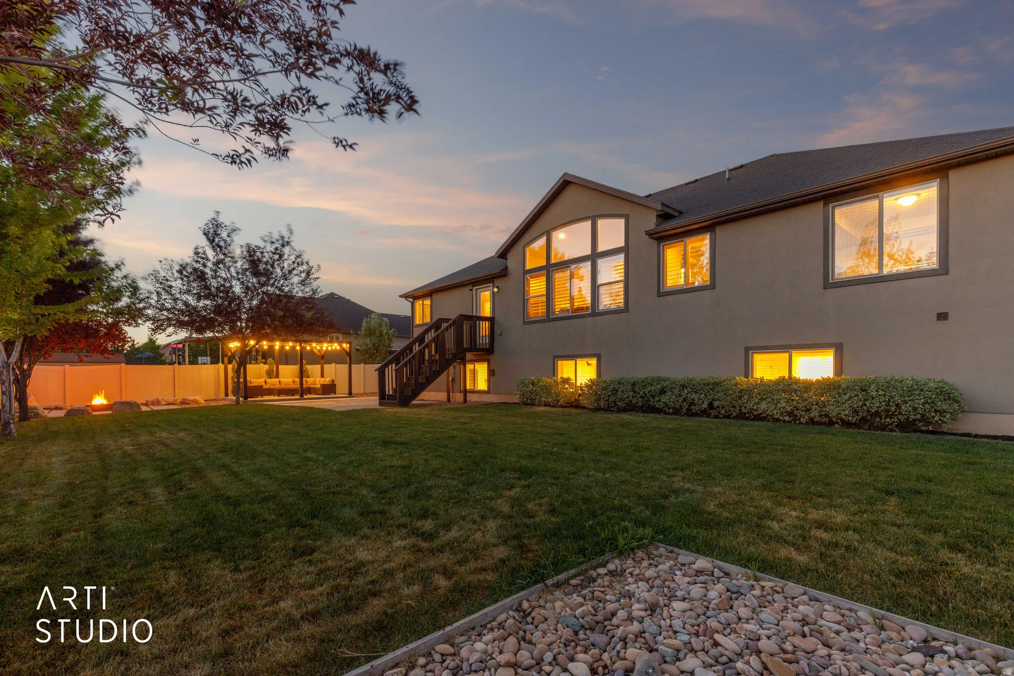 Expansive backyard featuring a manicured lawn, a string-lit pergola, and a visible fire pit area