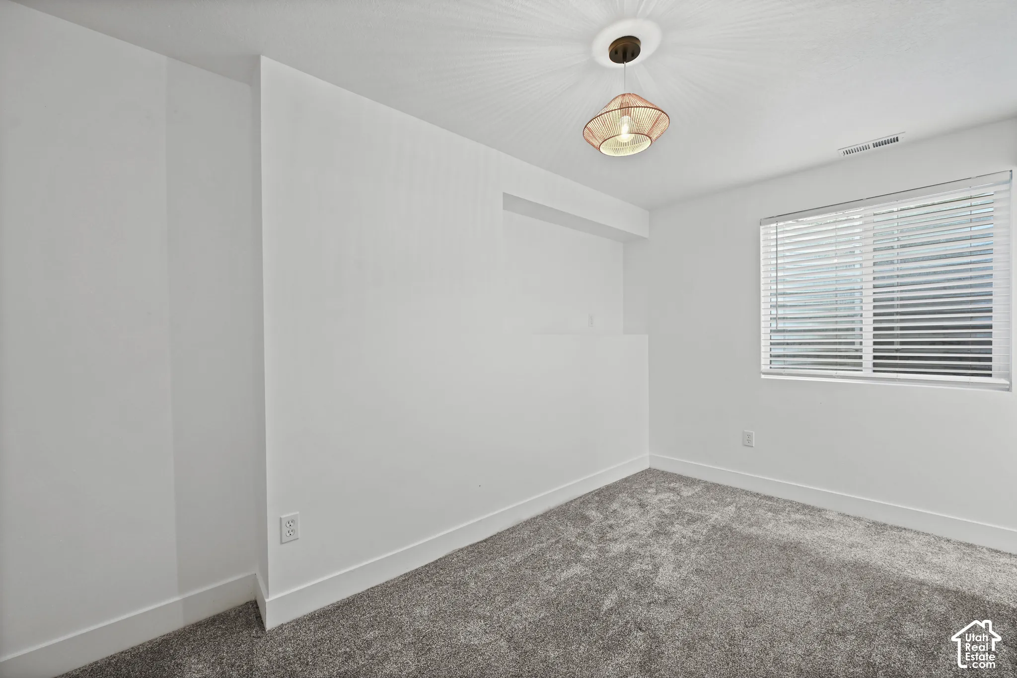 Carpeted room featuring a single window with horizontal blinds, a ceiling-mounted light fixture, and white baseboards