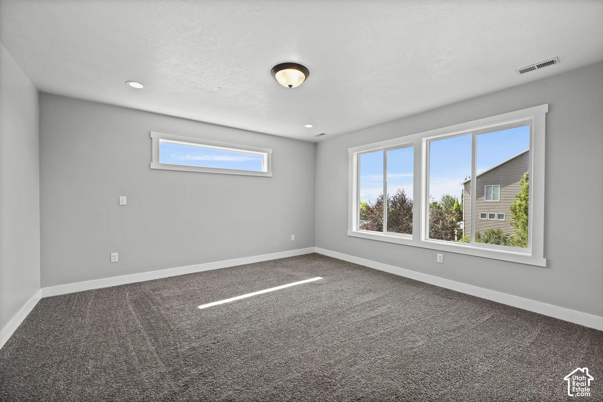 Spacious room featuring neutral carpeting, light gray walls, a large three-panel window, a high horizontal window, and recessed lighting