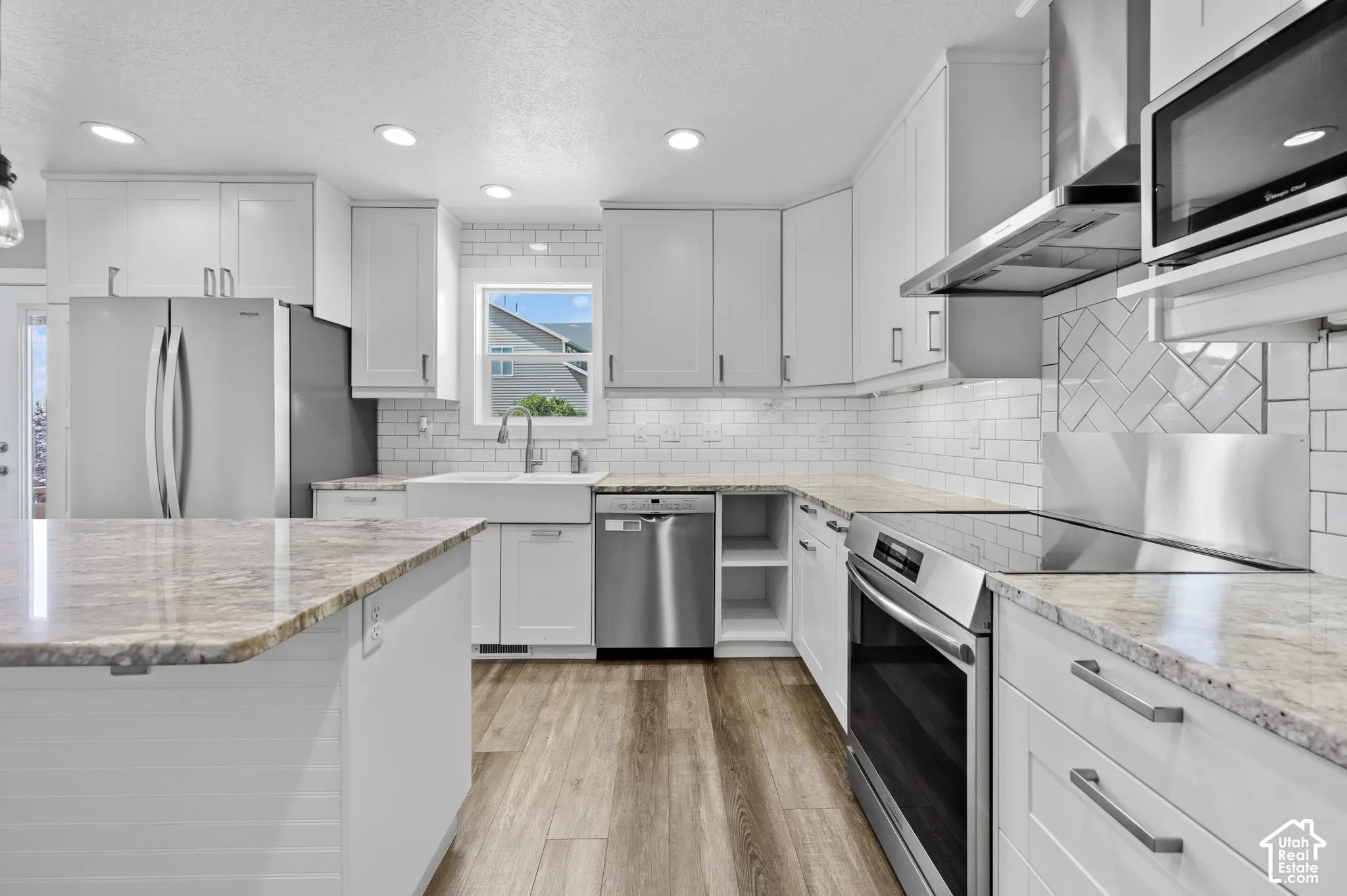 Contemporary kitchen featuring white cabinetry, stainless steel appliances, granite countertops, wood-finish flooring, and a subway tile backsplash