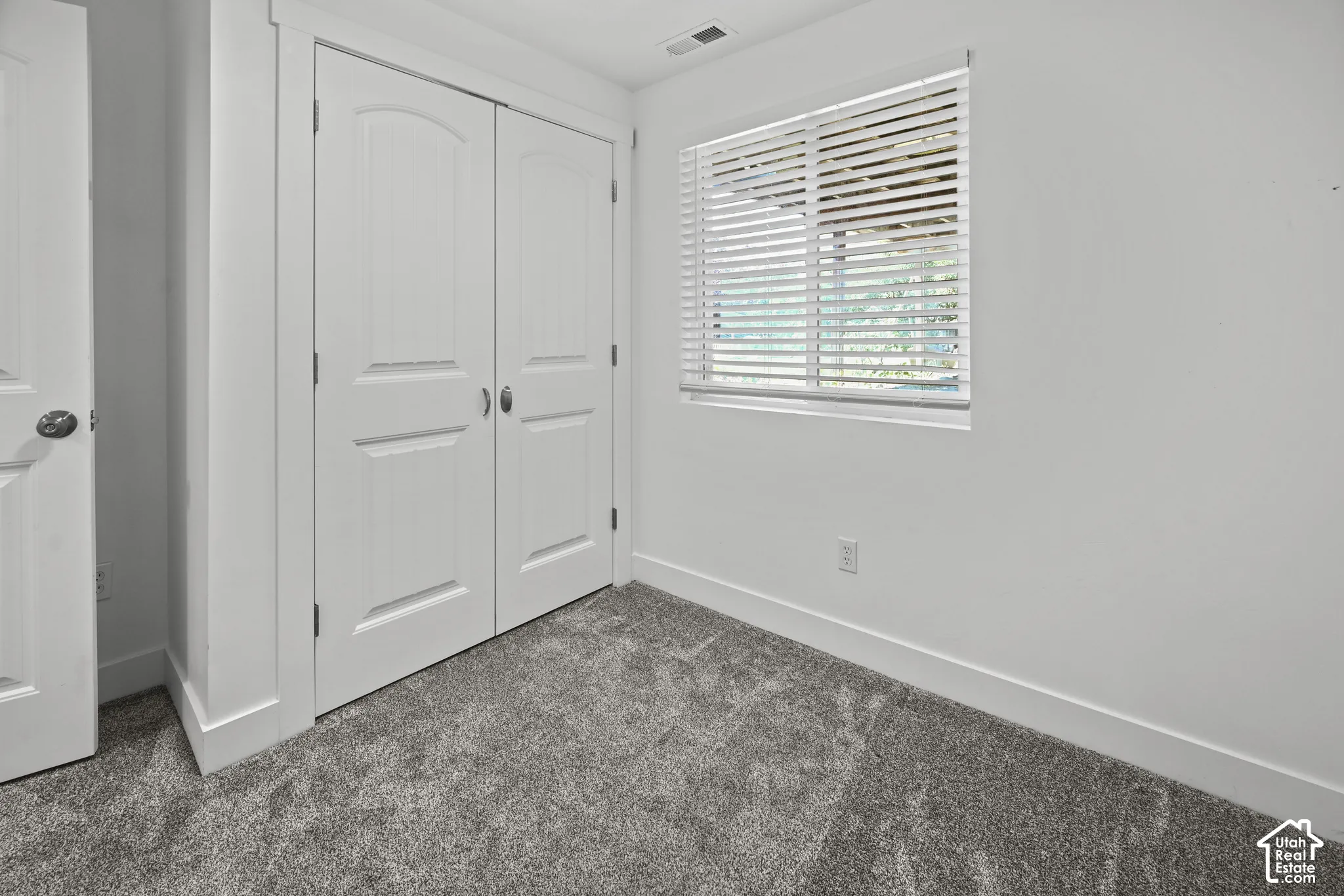 Interior room featuring textured grey carpeting, a double-door closet with arched paneling, and a single window with horizontal blinds