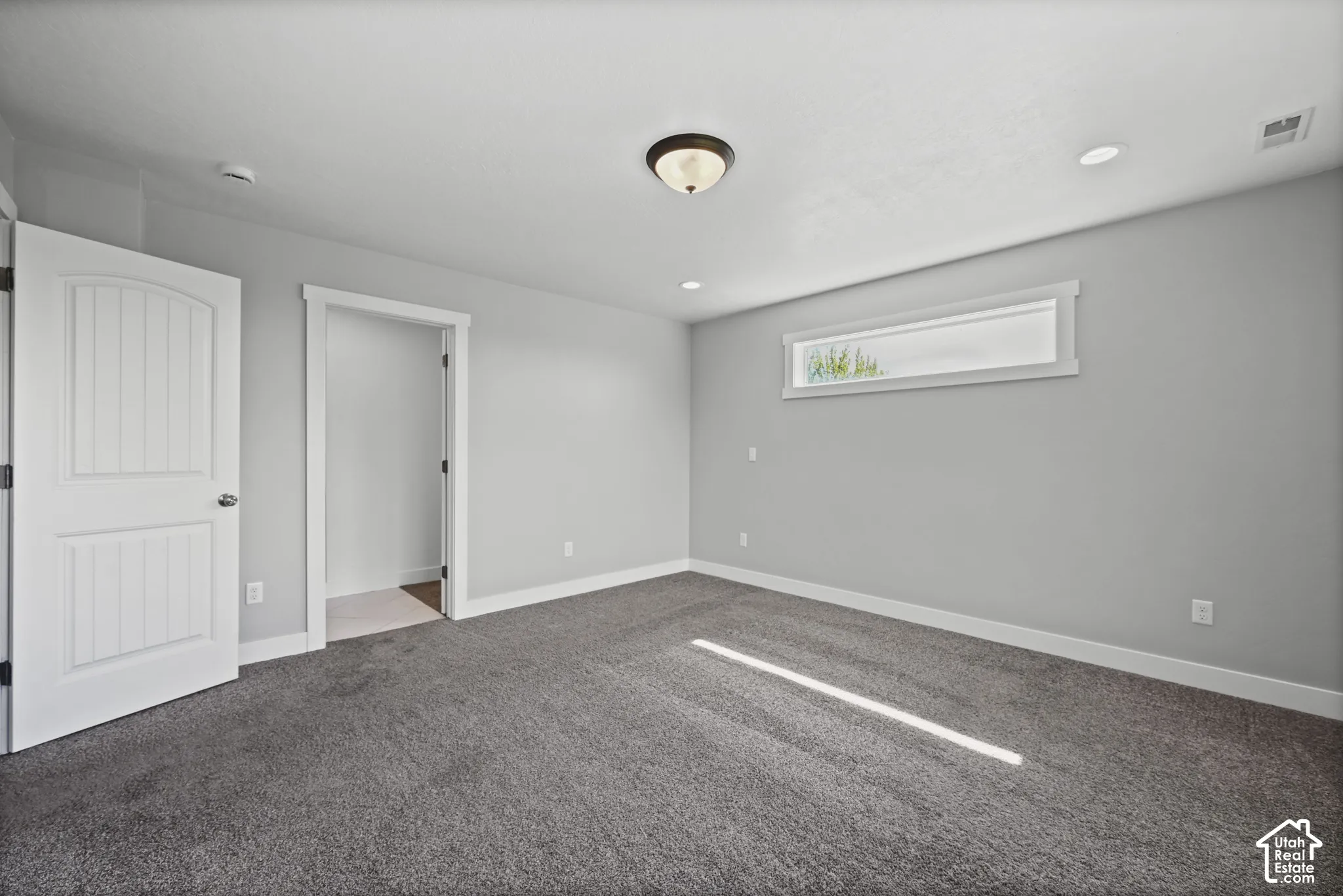 Spacious room featuring neutral gray walls, deep pile carpet, a horizontal transom window, recessed lighting, and a white paneled door