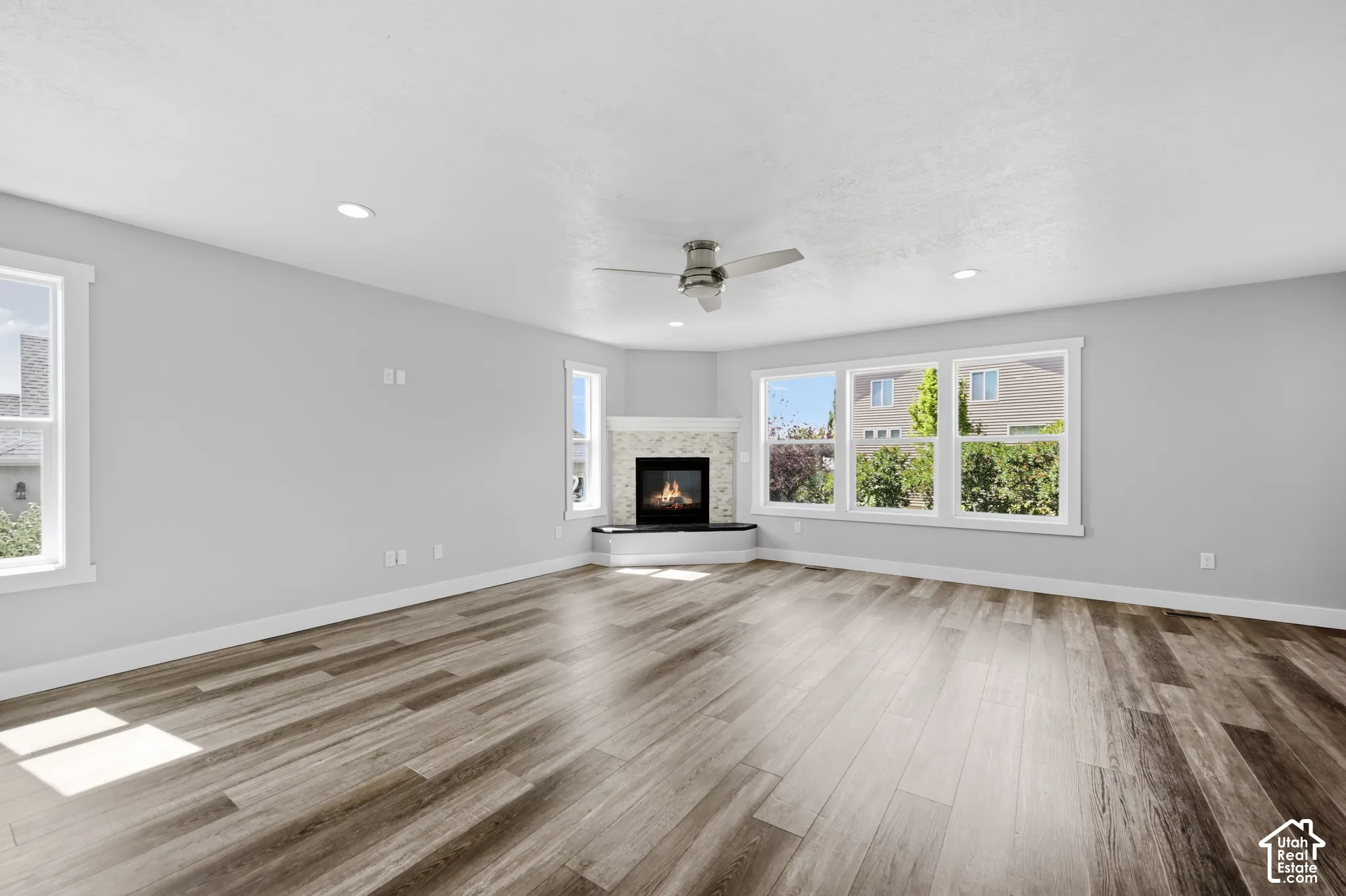Spacious living area featuring wood-finish flooring, a corner fireplace with a tiled surround, recessed lighting, and a ceiling fan