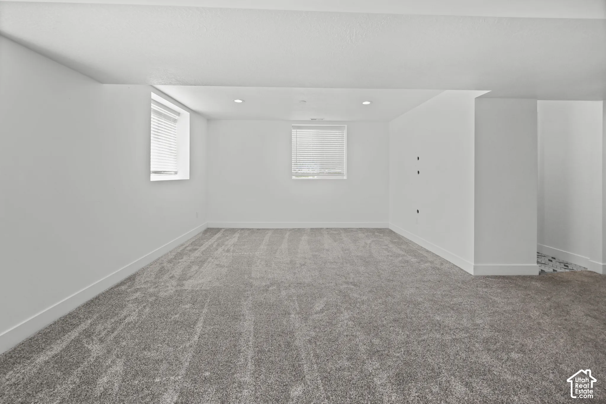 Spacious room featuring neutral carpeting, white walls, and two windows with blinds