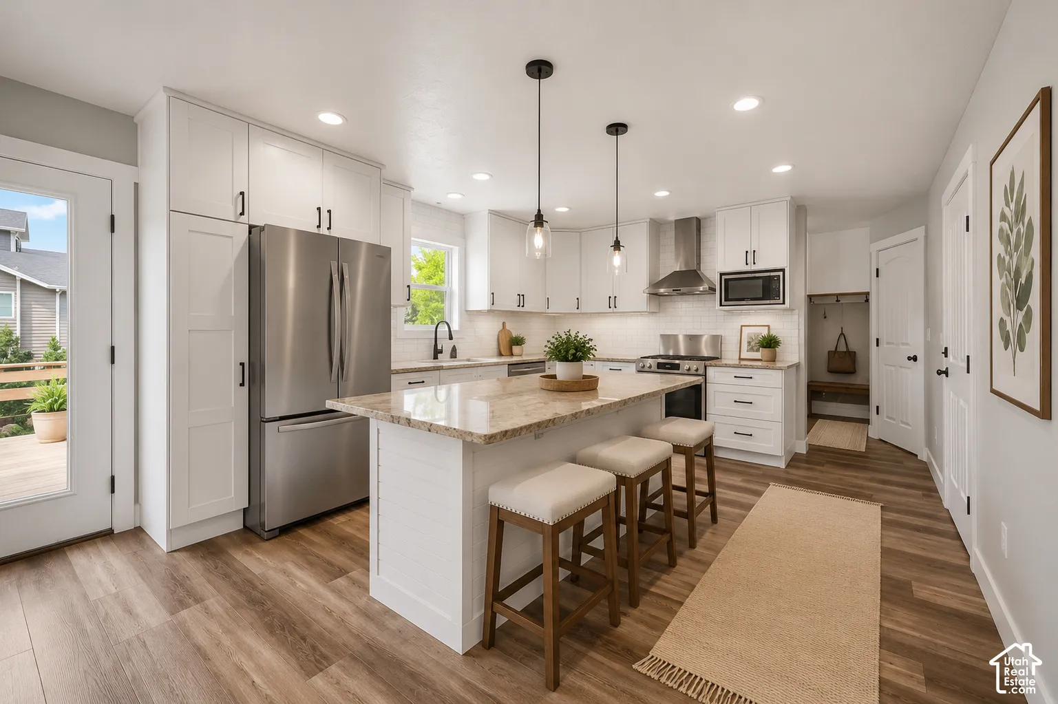 Open-concept kitchen featuring wood-finish flooring, white cabinetry, a central island with a light-toned countertop, stainless steel appliances, and recessed lighting