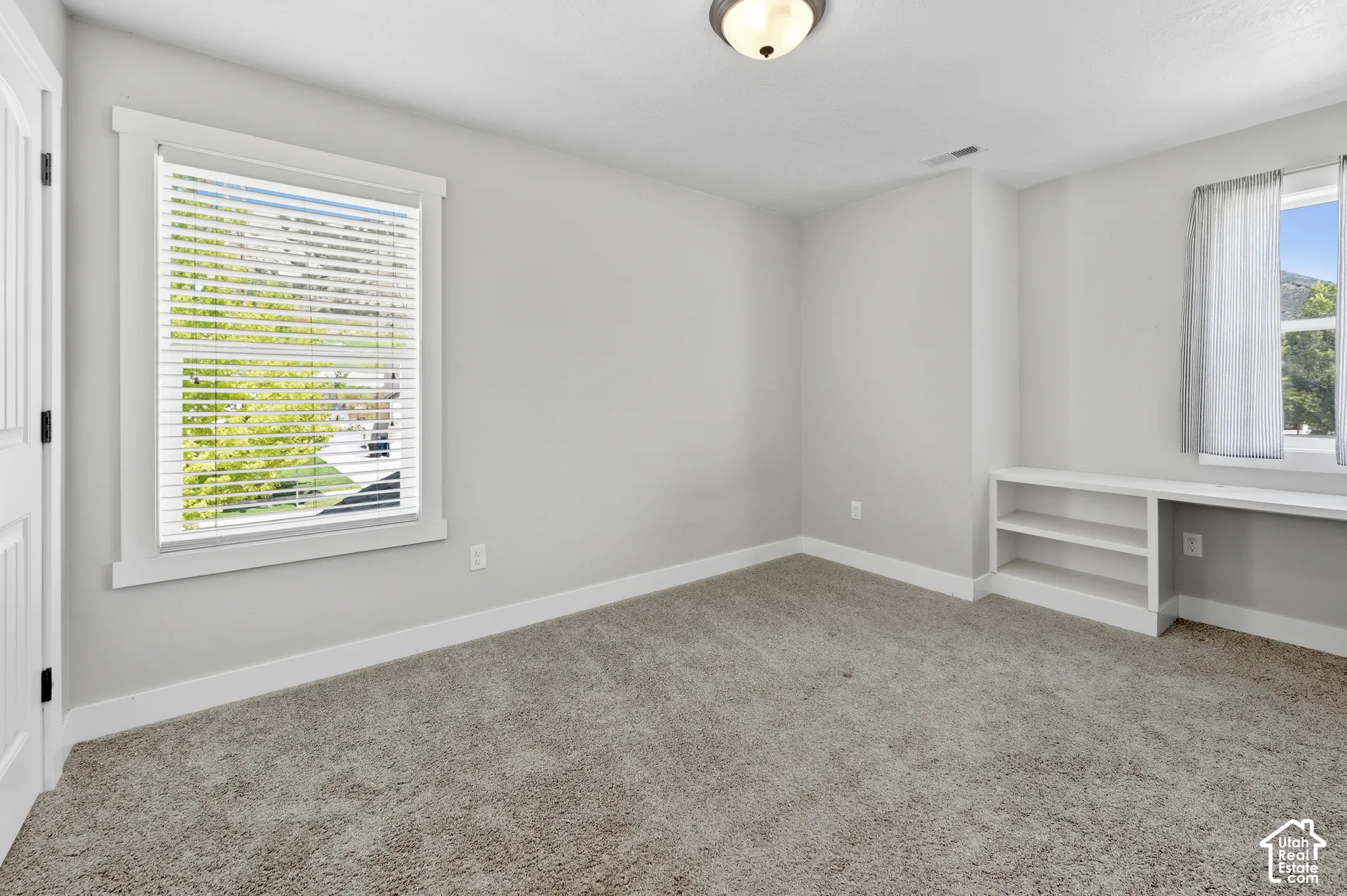 Carpeted room featuring a built-in shelving unit, a window with blinds, and white trim