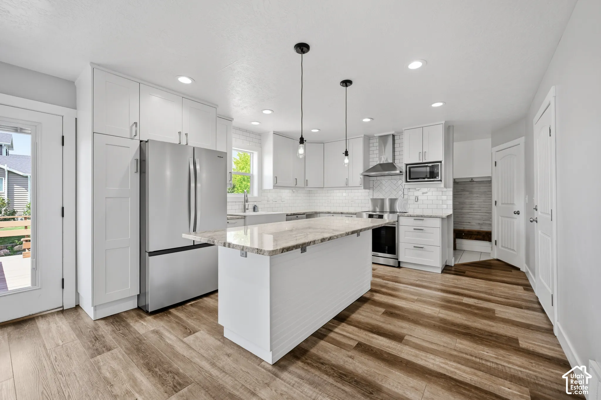 Modern kitchen featuring white cabinetry, stainless steel appliances, a center island with a light-toned countertop, wood-finish flooring, and a subway tile backsplash