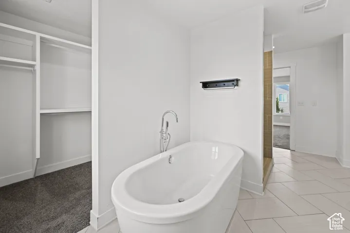Freestanding bathtub with floor-mounted faucet, herringbone tile flooring, and integrated shower stall with vertical tile detailing