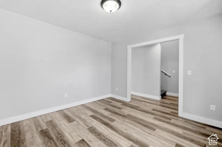 Open room featuring wood-finish flooring, light gray wall paint, white baseboards, and a semi-flush ceiling light fixture