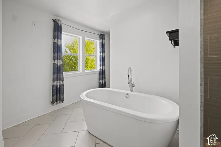 Freestanding oval soaking tub featuring a floor-mounted chrome faucet, set against a backdrop of bright windows with patterned curtains