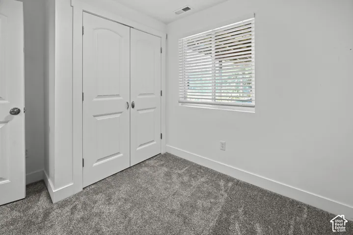 Interior room featuring textured grey carpeting, a double-door closet with arched paneling, and a single window with horizontal blinds