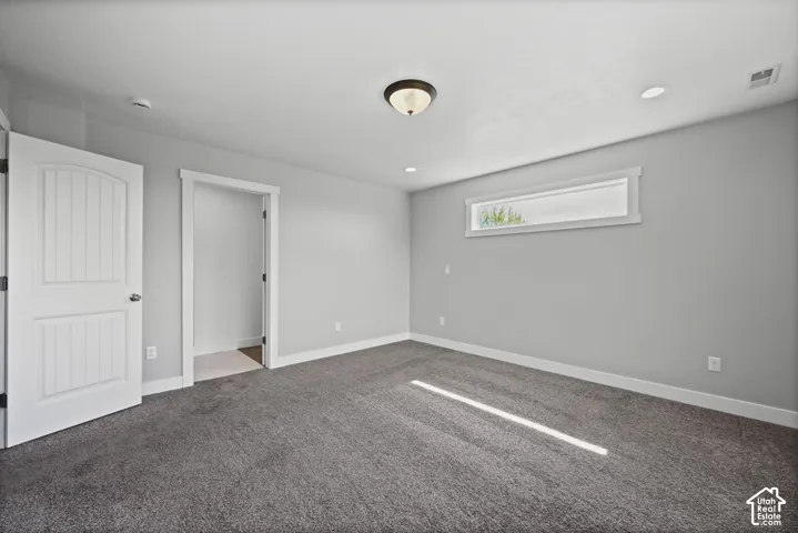 Spacious room featuring neutral gray walls, deep pile carpet, a horizontal transom window, recessed lighting, and a white paneled door