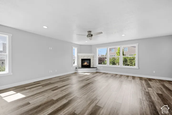 Spacious living area featuring wood-finish flooring, a corner fireplace with a tiled surround, recessed lighting, and a ceiling fan