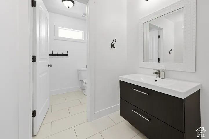 Bathroom featuring a floating dark wood-finish vanity with an integrated white sink, a decorative framed mirror, and light-toned tile flooring