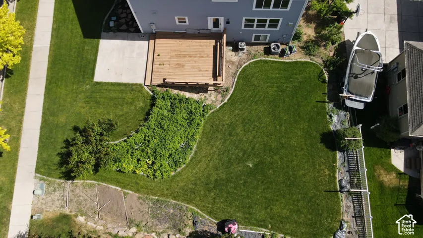 Expansive backyard featuring a manicured lawn, a wood deck, a concrete patio, and garden beds