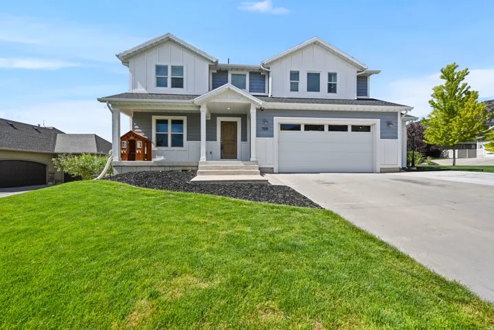 Contemporary two-story residence featuring a two-car garage, white vertical siding, blue horizontal siding, a covered porch, and a concrete driveway