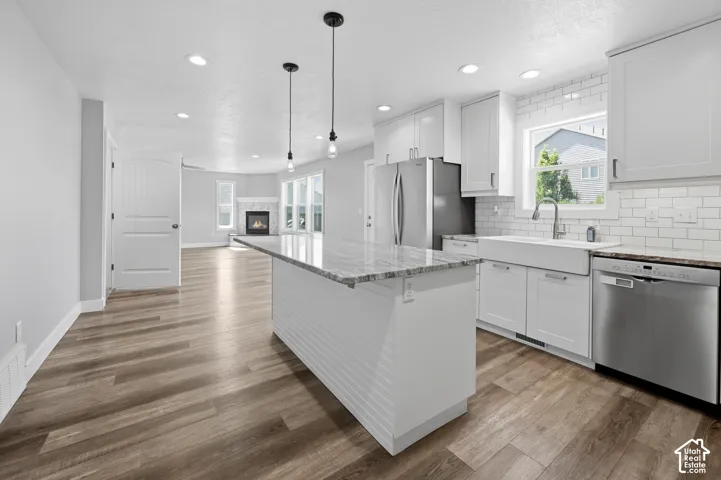 Modern kitchen featuring a large center island with a granite-style countertop, white shaker cabinetry, stainless steel appliances, and a farmhouse sink