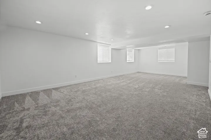 Spacious room featuring new gray carpet, white walls, recessed ceiling lighting, and multiple windows with blinds