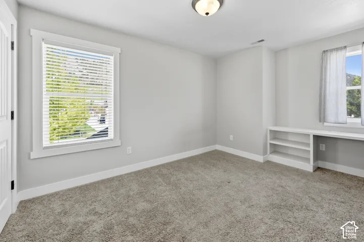 Carpeted room featuring a built-in shelving unit, a window with blinds, and white trim