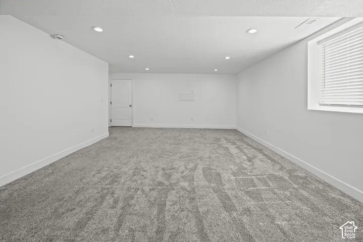 Spacious room featuring gray carpeting, white walls, recessed ceiling lights, a white interior door, and a window with horizontal blinds