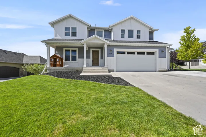 Contemporary two-story residence featuring a two-car garage, white vertical siding, blue horizontal siding, a covered porch, and a concrete driveway