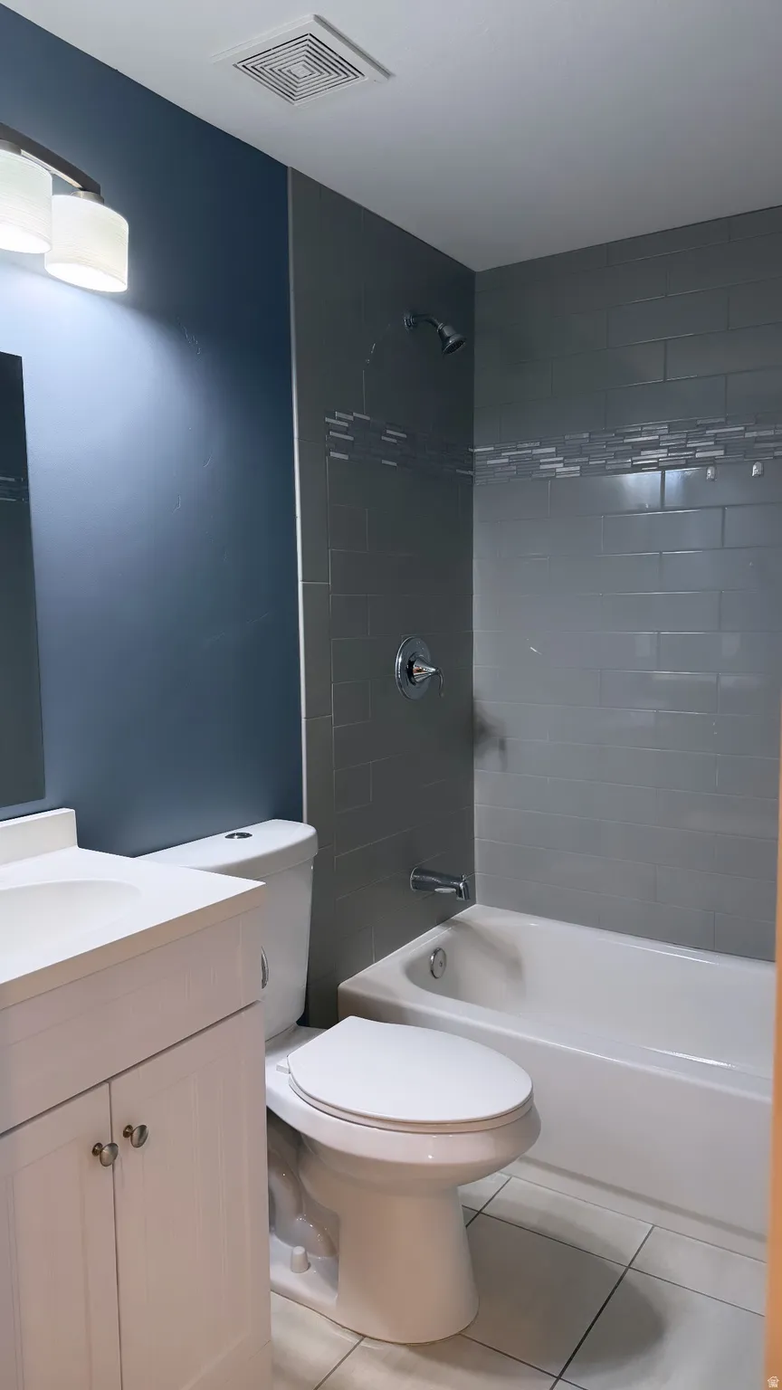 Bathroom featuring a white vanity with integrated sink, a white toilet, and a bathtub with subway tile surround