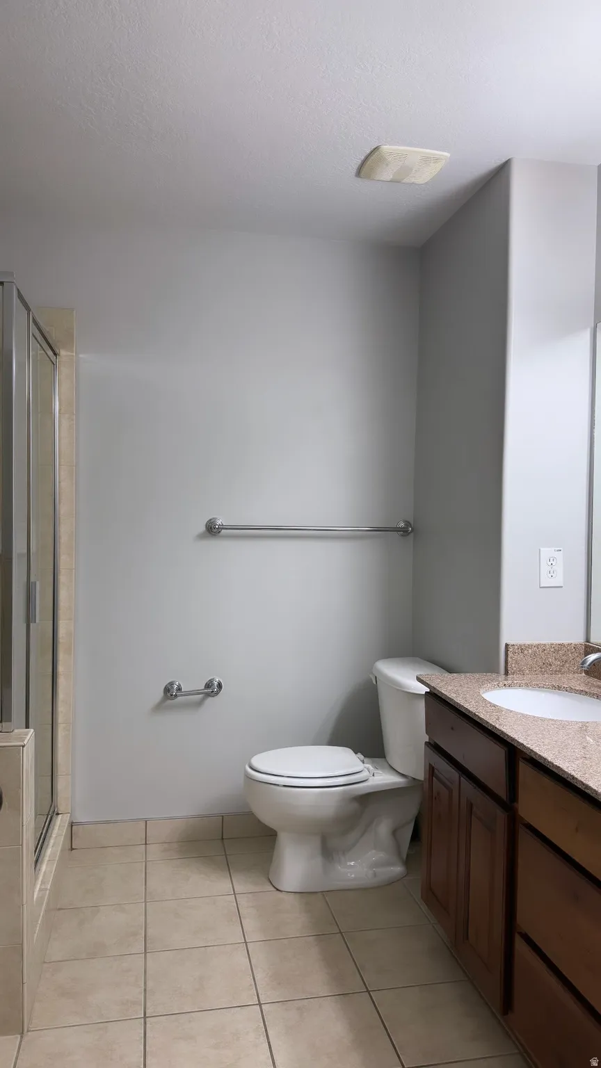Bathroom featuring a glass-enclosed shower, tiled flooring, built-in vanity with a countertop, toilet, and wall-mounted towel bars