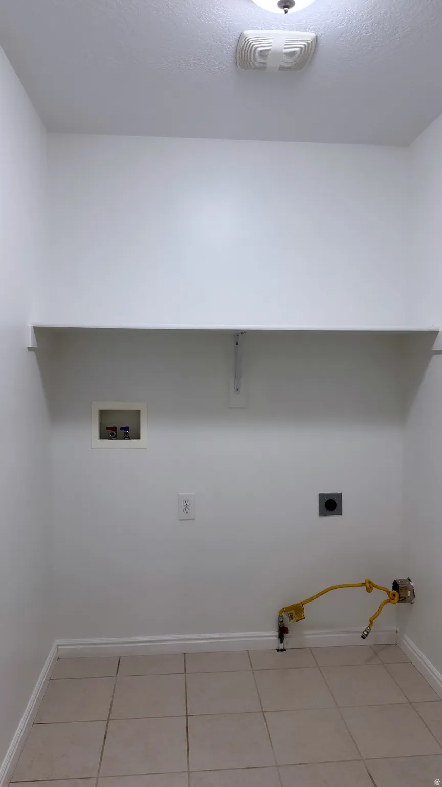 Utility room with tiled flooring, baseboards, and a wall-mounted shelf