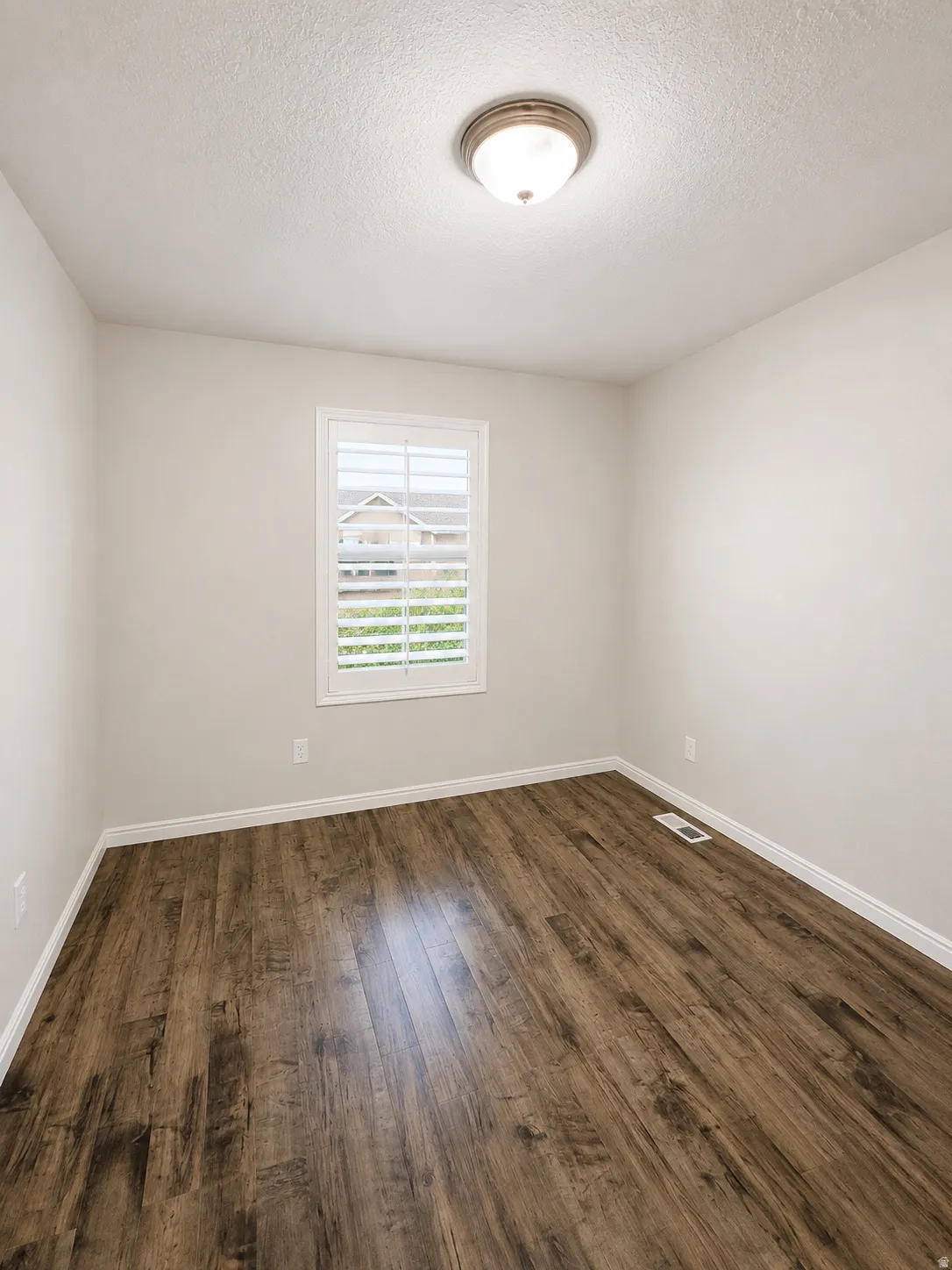 Interior room featuring wood-finish flooring, light-toned walls, a window with plantation shutters, and a flush-mount ceiling light fixture