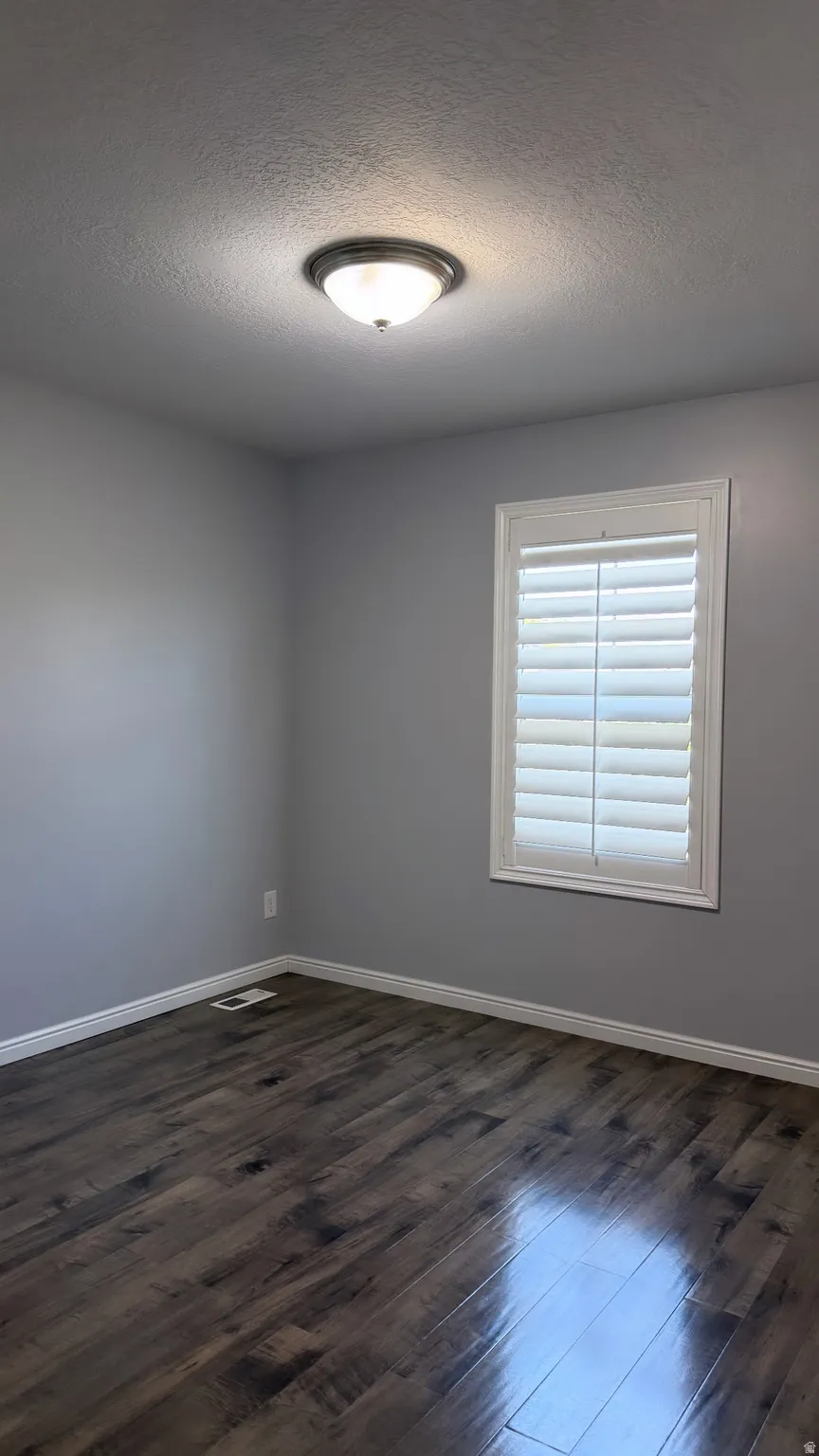 Room featuring wood-finish flooring, a contemporary flush-mount light fixture, and a window with white plantation shutters