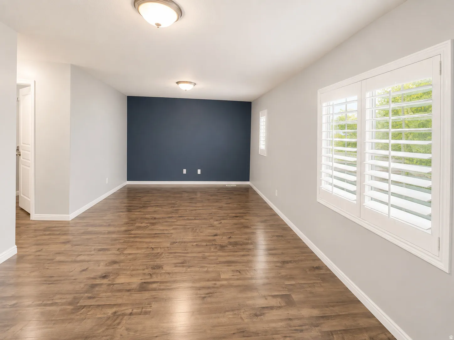 Spacious interior room featuring wood-finish flooring, light gray walls, and a contrasting deep blue accent wall