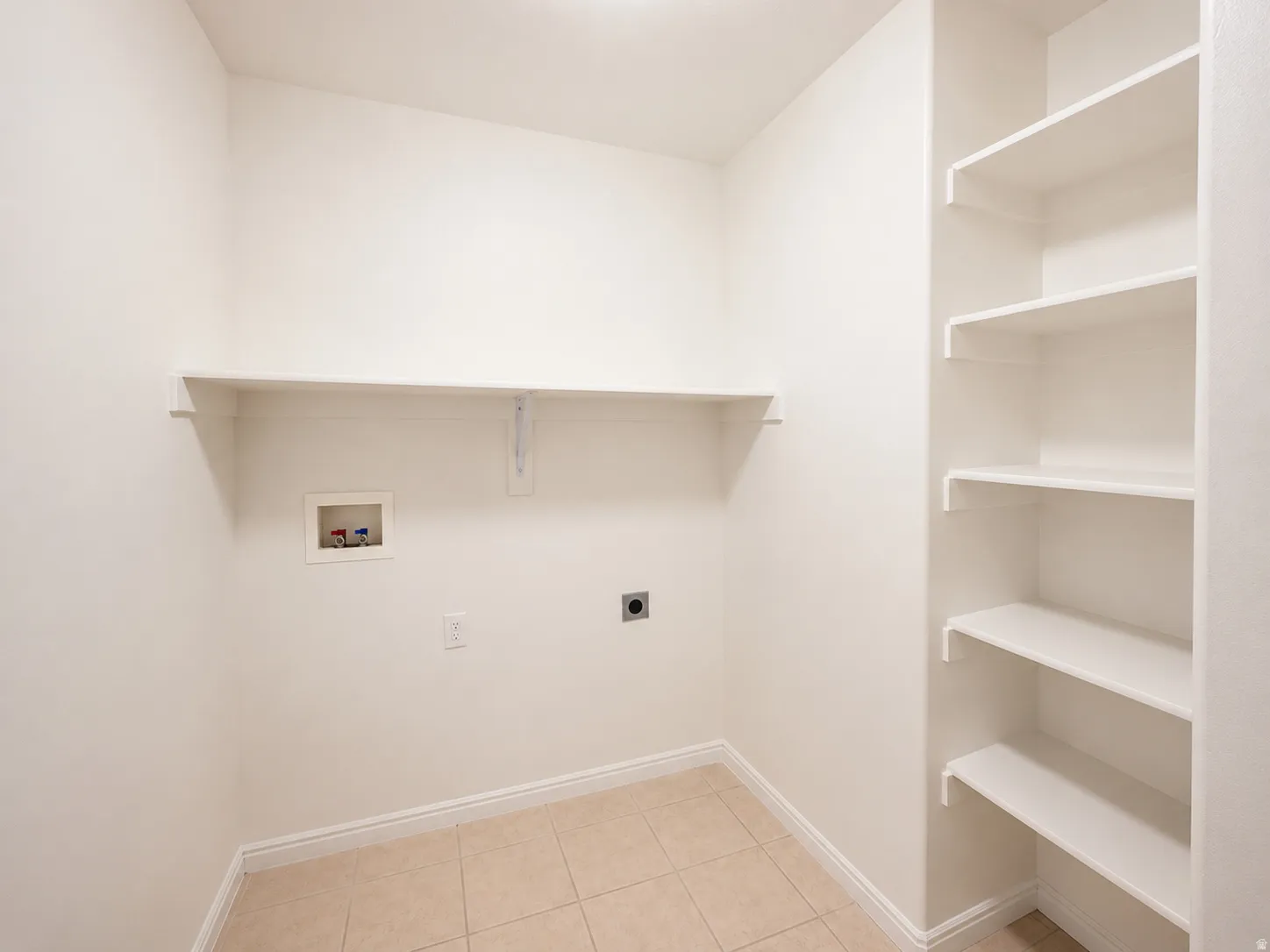 Dedicated utility space featuring built-in shelving, a wall-mounted shelf, tiled flooring, baseboard trim, and a washer/dryer hookup