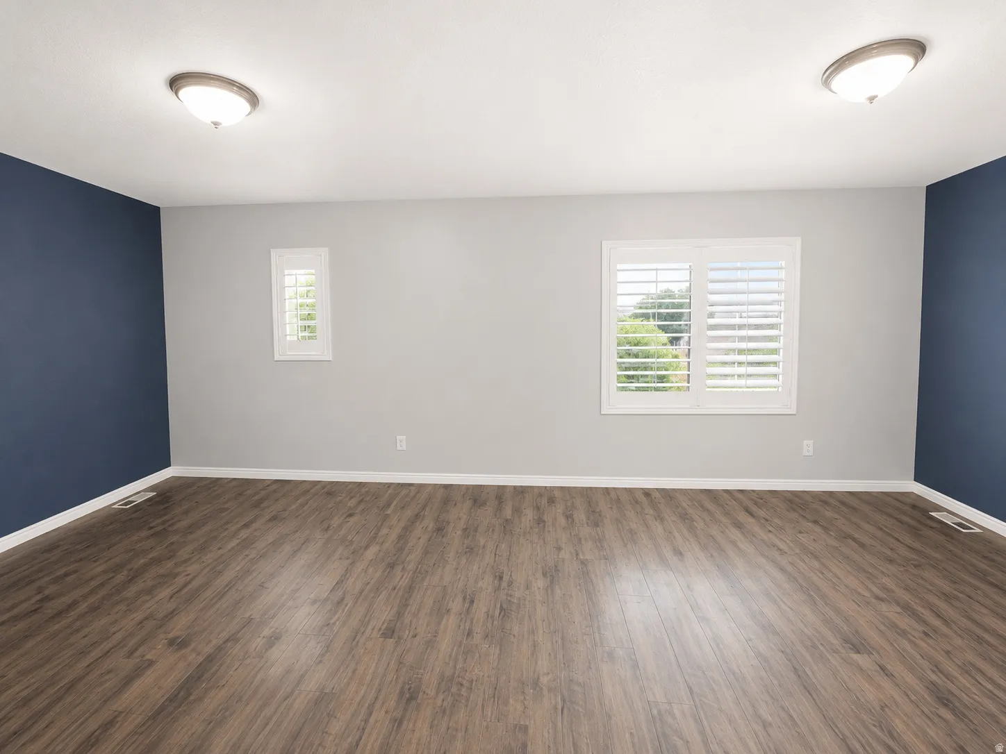 Spacious room featuring wood-finish flooring, white baseboards, and a neutral wall color with two accent walls