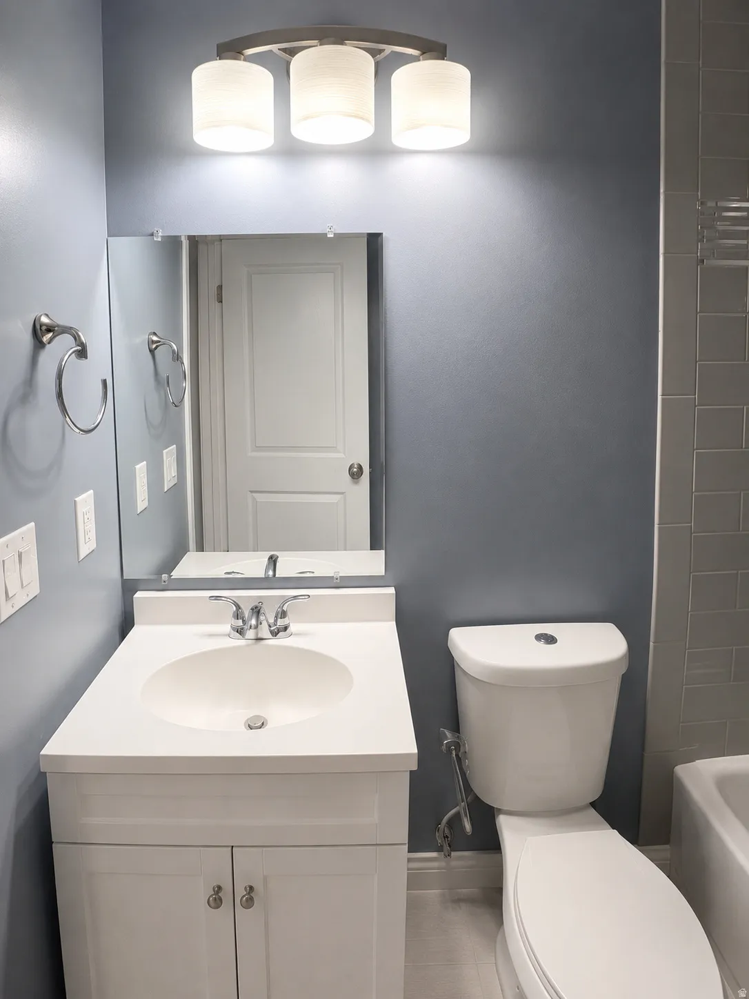 Bathroom featuring a white vanity with integrated sink, chrome faucet, wall-mounted mirror, and three-light fixture