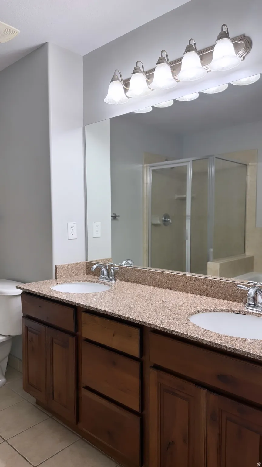 Double vanity with brown wood cabinetry, light-colored speckled countertop, and under-mount sinks