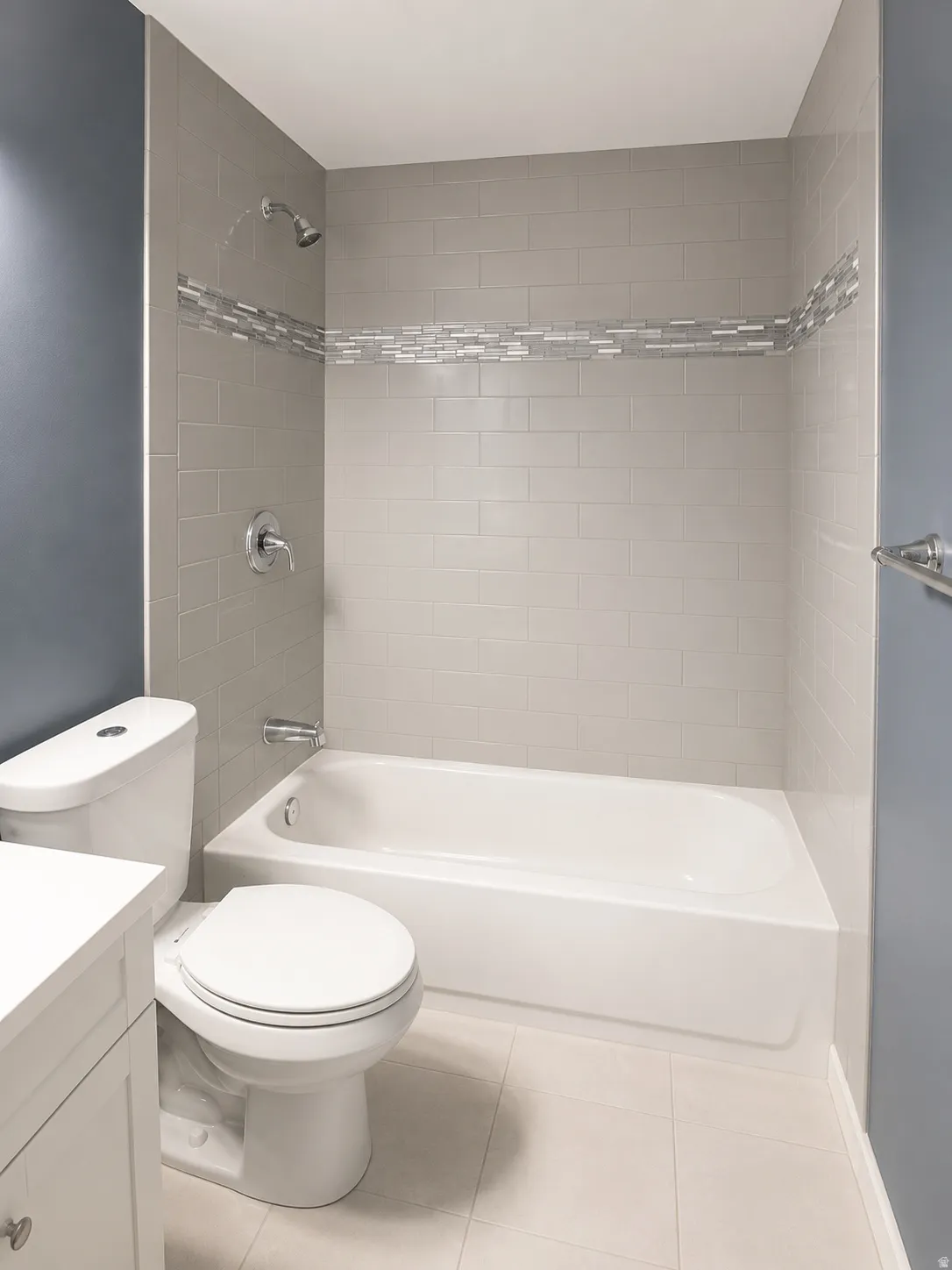 Full bathtub and shower combination featuring subway tile surround with decorative accent band, chrome fixtures, and a white toilet