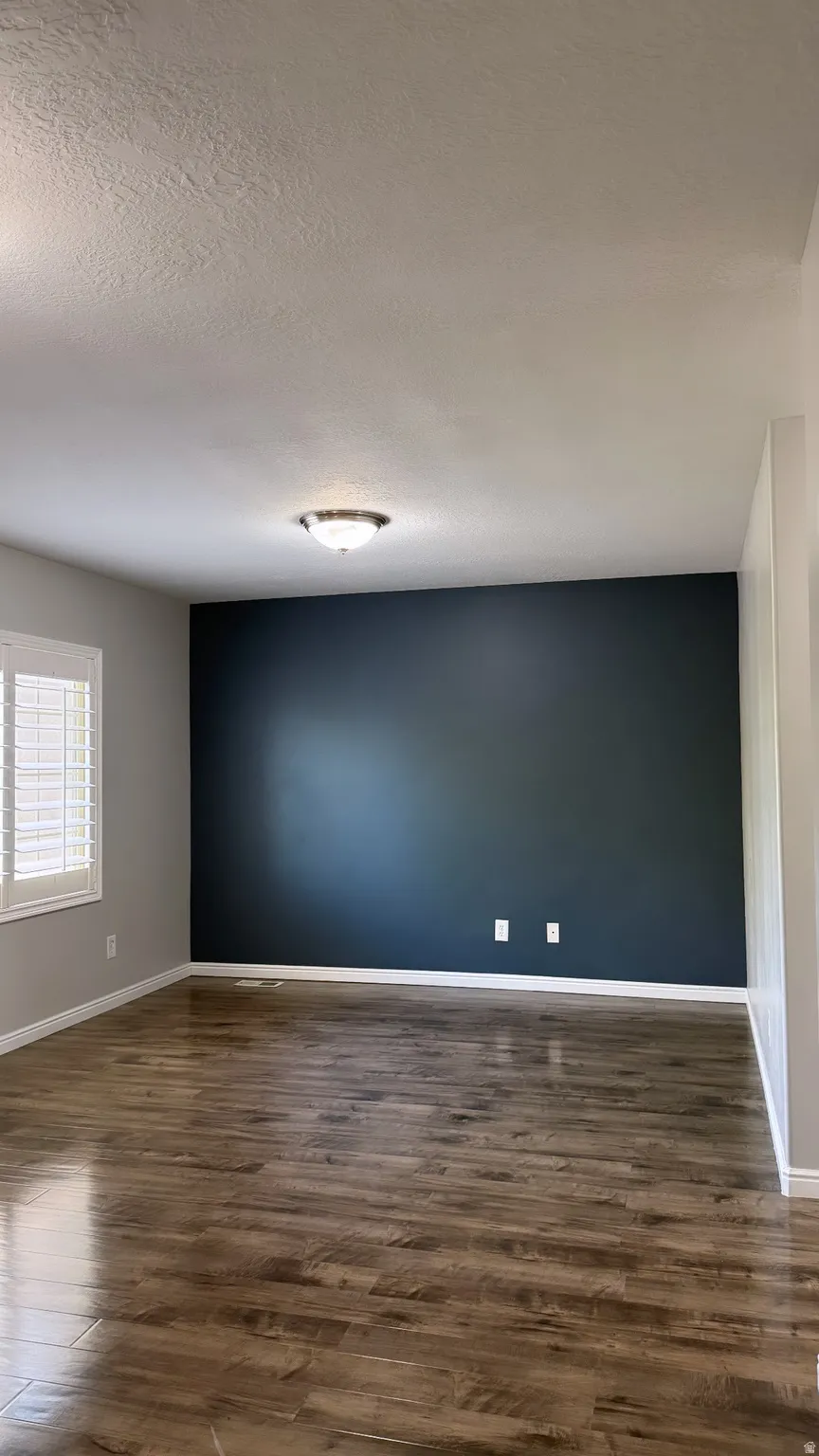 Spacious room featuring wood-finish flooring, a feature wall, white baseboards, and window with plantation shutters