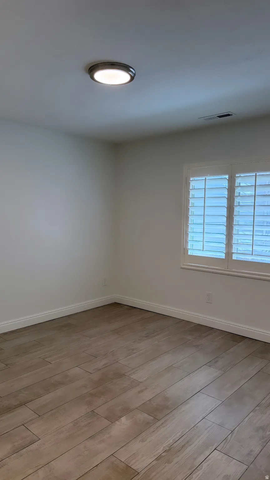Room featuring wood-look tile flooring, white baseboards, and a window with plantation shutters