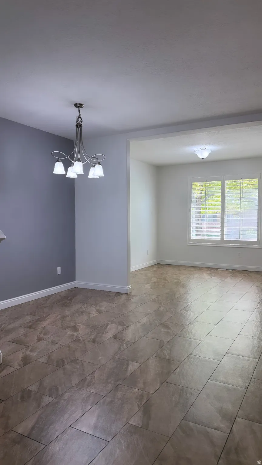 Spacious interior featuring large format floor tiling, a five-light chandelier, and multiple windows with plantation shutters