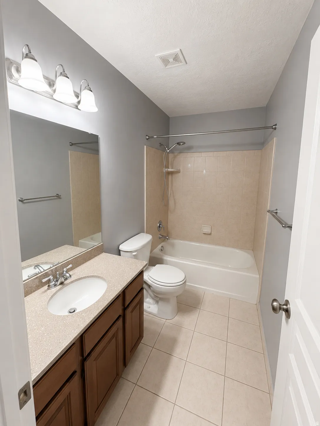 Bathroom featuring a light-colored tile floor, a vanity with a light-speckled countertop and wood-finish cabinetry, a toilet, and a bathtub with a tile surround