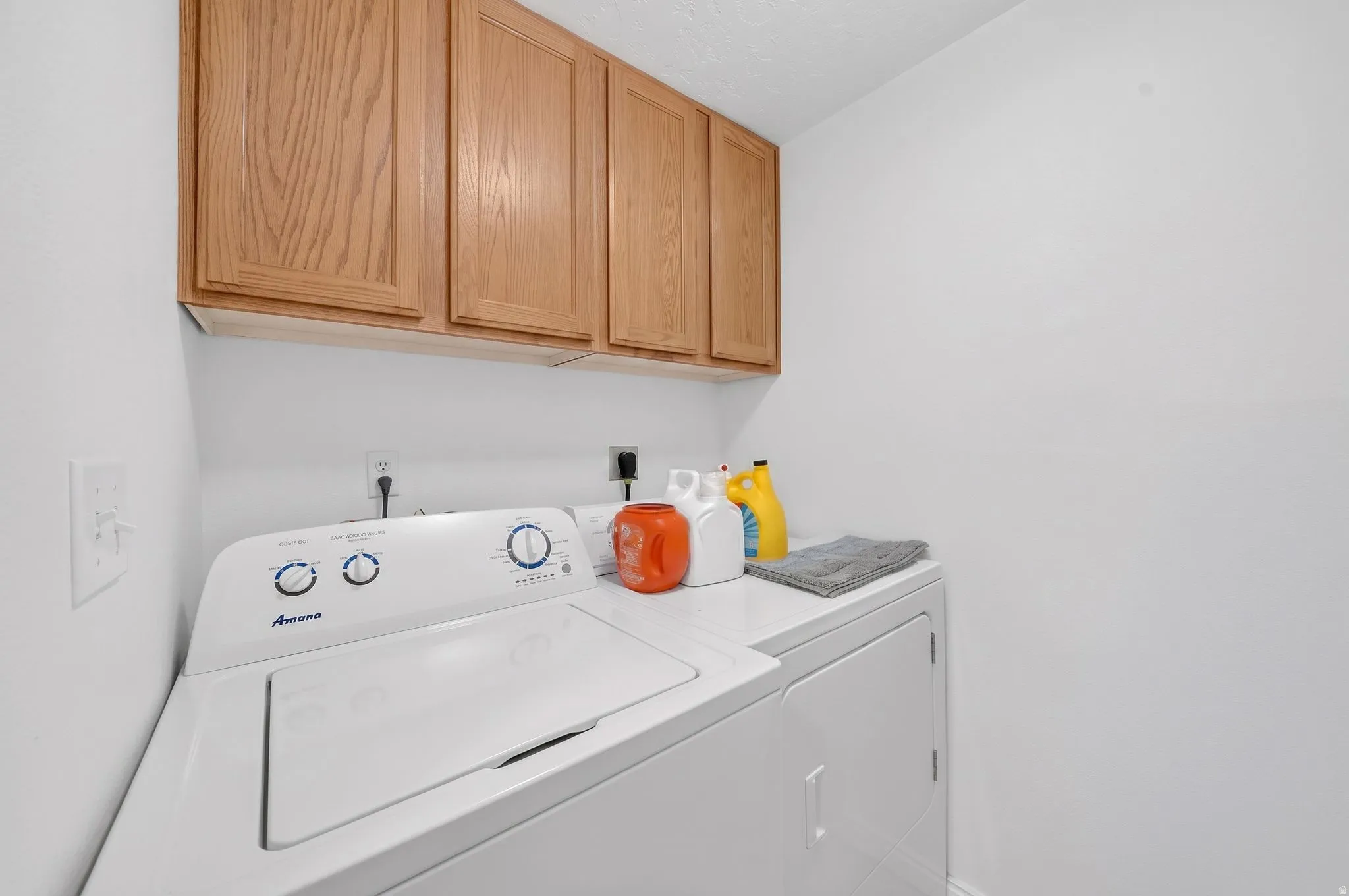 Laundry area featuring white walls and upper wood cabinetry