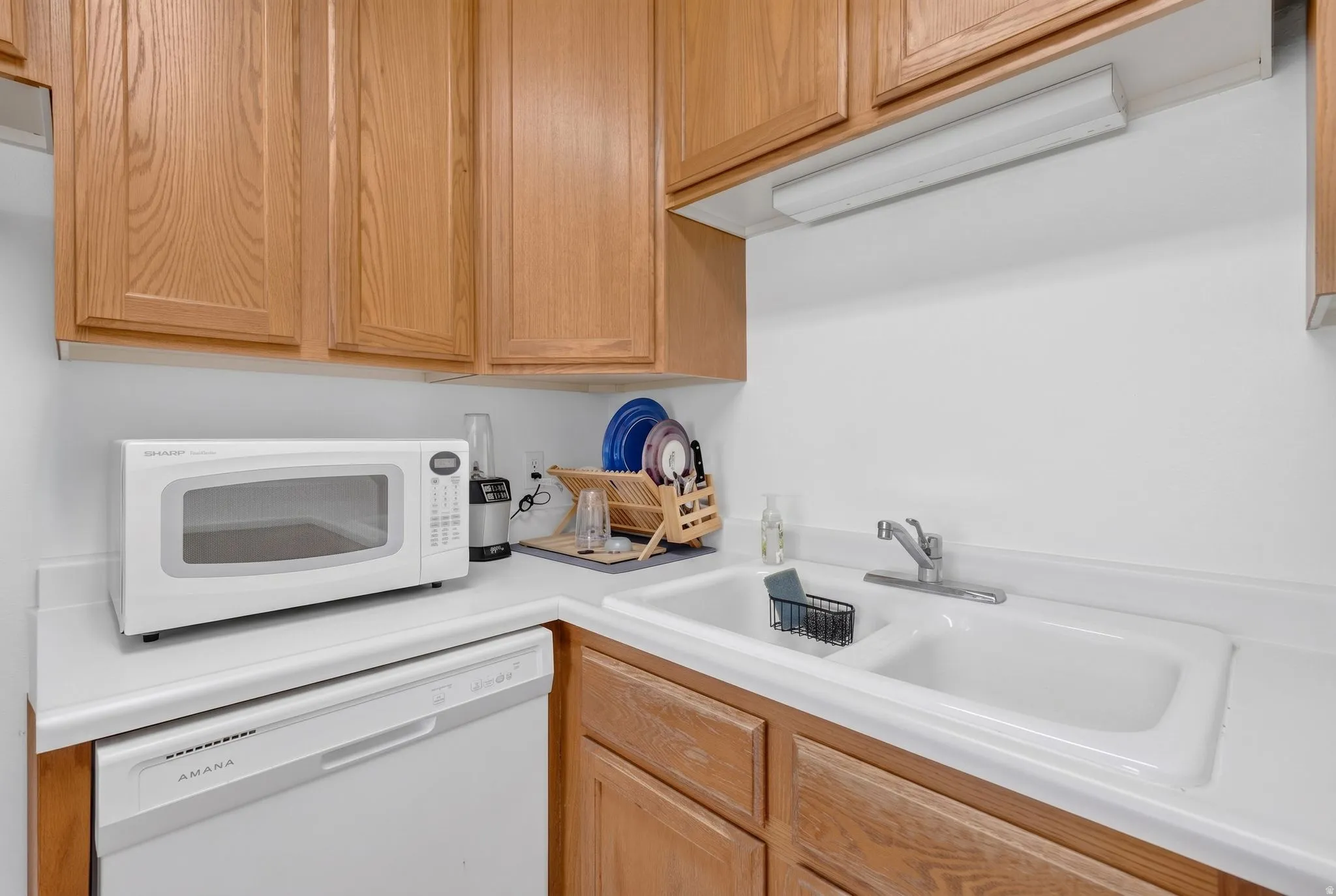 Kitchen area featuring a double-basin sink with a chrome faucet, light wood cabinetry, white countertops, and a built-in dishwasher